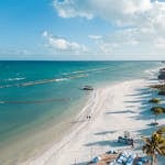 A beautiful aerial view of Playa del Carmen's white sandy beach with clear blue waters and palm trees swaying in the tropical breeze.
