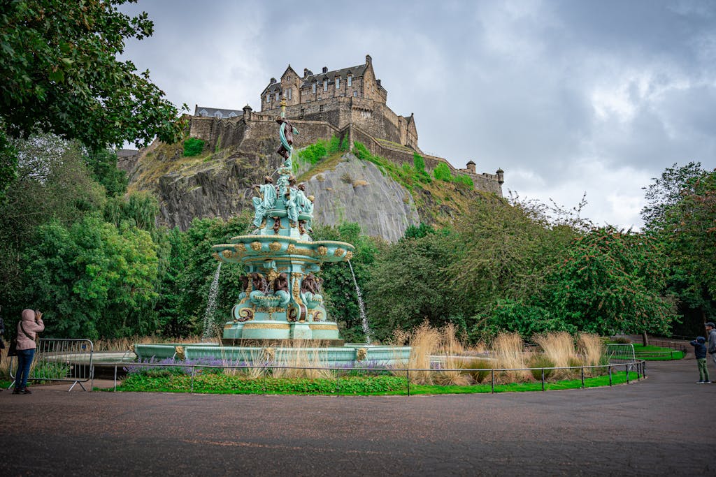 Beautiful view of Edinburgh Castle and Ross Fountain surrounded by lush greenery in Scotland.