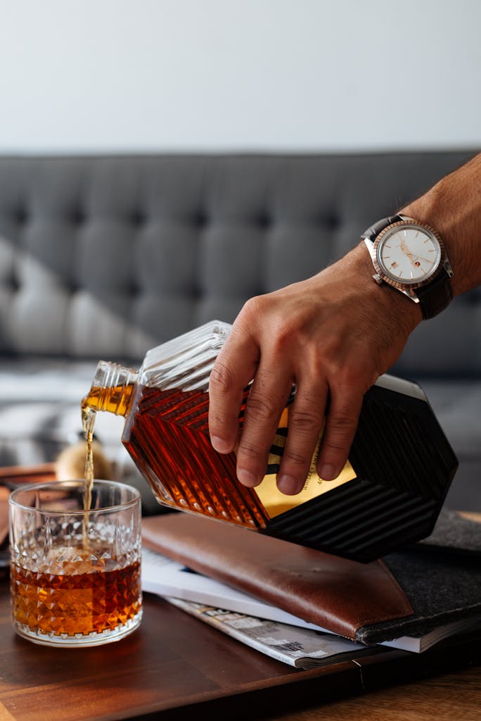 Close-up of a hand pouring whiskey from a bottle into a glass indoors.