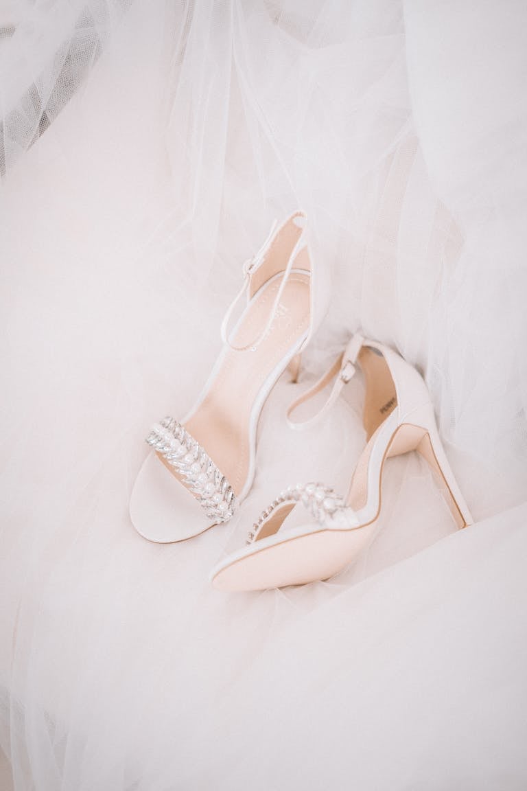Close-up of elegant white wedding heels adorned with pearls on a flowing gown.