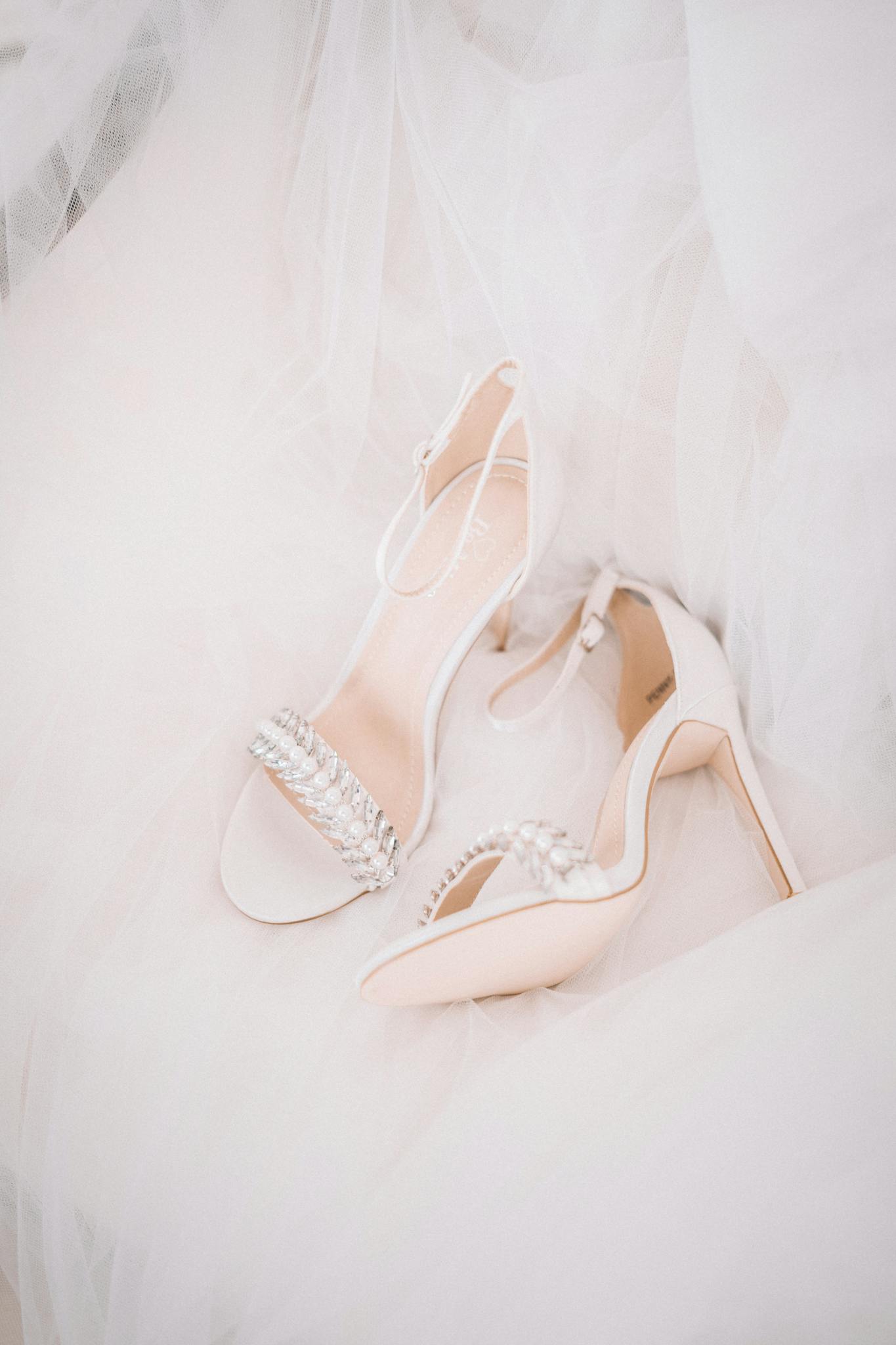 Close-up of elegant white wedding heels adorned with pearls on a flowing gown.