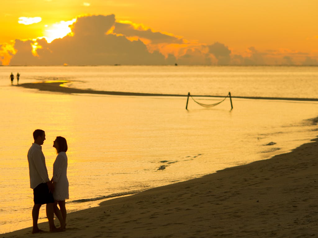 A couple enjoys a romantic moment on a tropical beach at sunset, symbolizing love and adventure.
