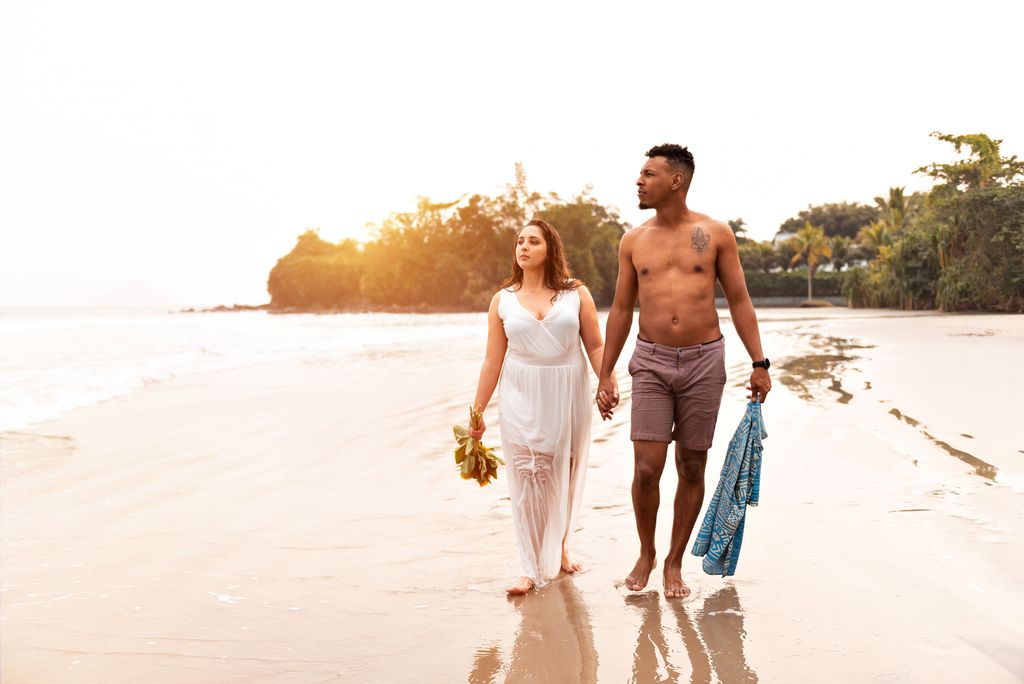 A couple strolls hand in hand along a serene São Sebastião beach during a warm sunset.