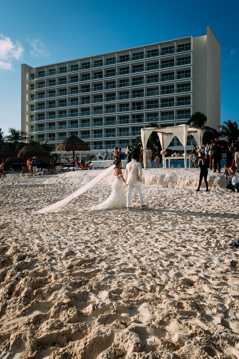A stunning beach wedding with the bride and groom on a sandy shore in front of a resort hotel.