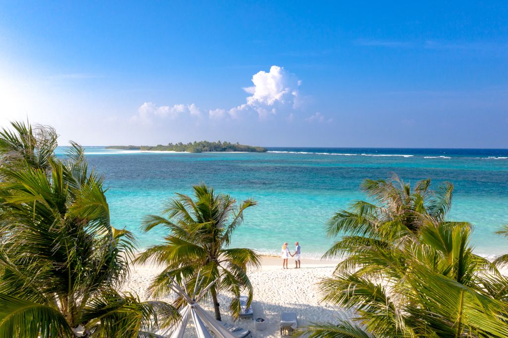Aerial view of a couple on a pristine tropical beach with turquoise waters.