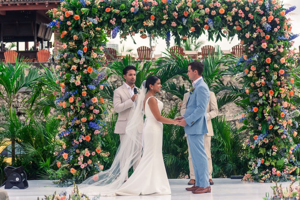 Beautiful outdoor wedding under a vibrant floral arch, capturing a couple exchanging vows.