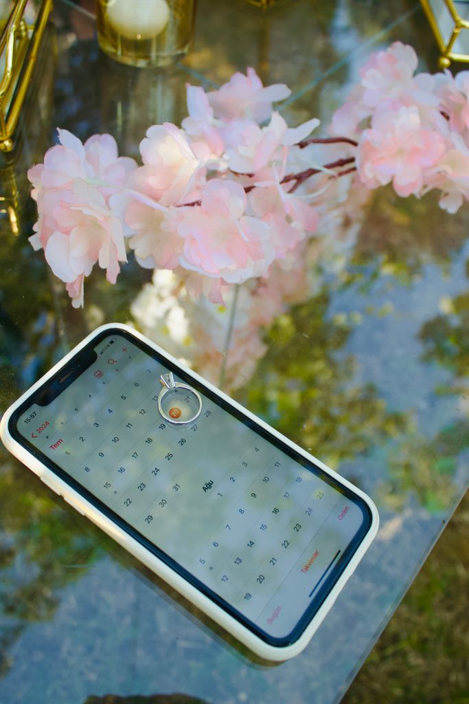 Engagement ring on smartphone calendar with pink flowers. Perfect for proposals and wedding planning visuals.