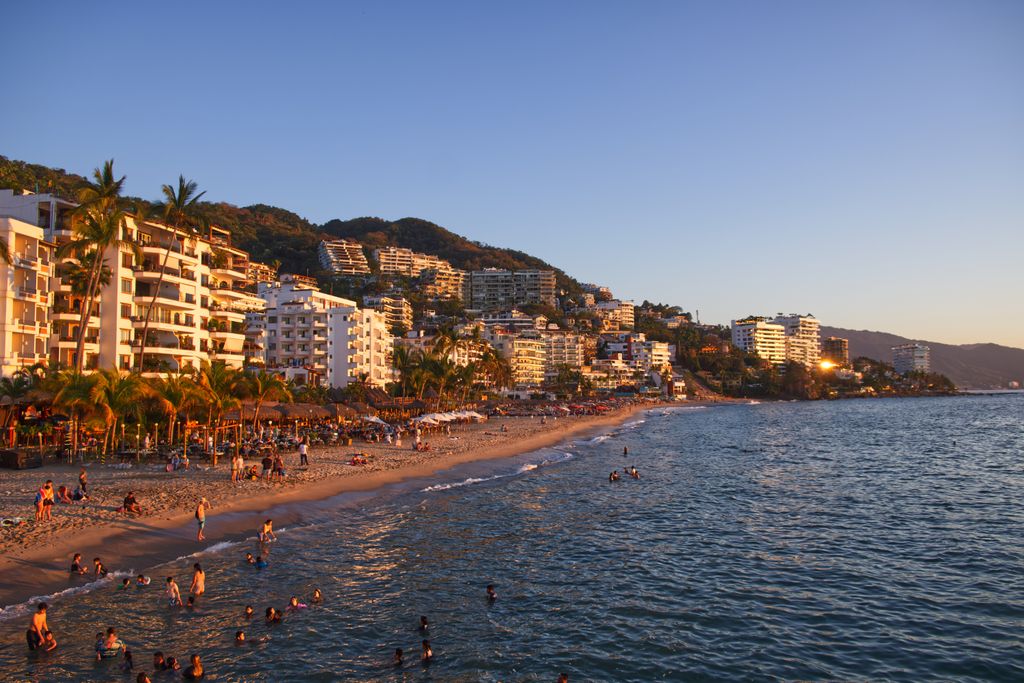 Explore the vibrant coastline of Puerto Vallarta, Mexico with bustling beach activity and scenic resorts at sunset.