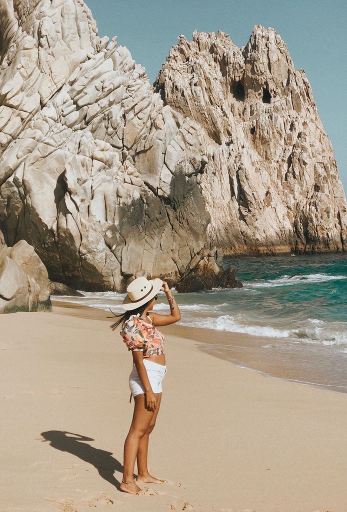 Woman standing on sandy beach at Cabo San Lucas with stunning rock formations and ocean view.