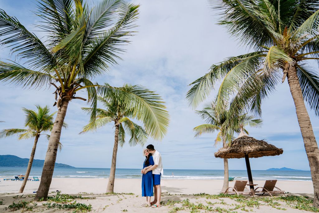 A couple embraces on a sandy beach under palm trees, capturing a romantic moment.