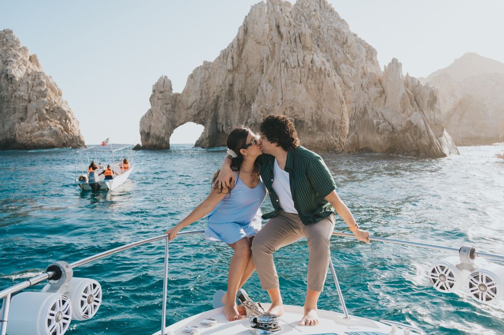 A couple shares a romantic kiss on a boat near the iconic Arch of Cabo San Lucas, Mexico.