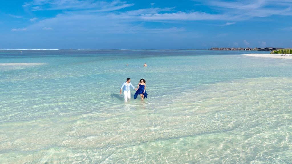 A couple strolling through crystal-clear water on a sunny day in the Maldives.