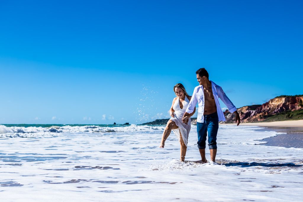 Couple enjoying a romantic walk on a sunny beach in Brazil, splashing in the waves.