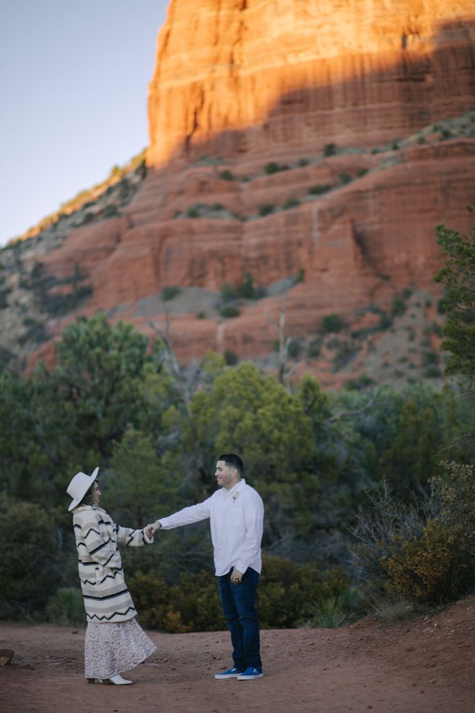 A couple holding hands in front of Sedona's iconic red rock formations, embracing nature.