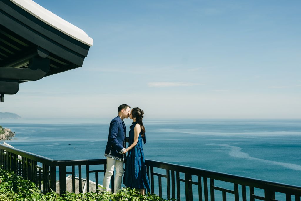 A couple shares a kiss on a balcony with a stunning ocean view, symbolizing love and romance.