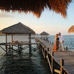 A couple shares a romantic moment on a wooden pier under thatched roofs in East Nusa Tenggara, Indonesia.