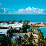 Aerial view of a luxurious beachfront resort with palm trees, pool, and ocean view.